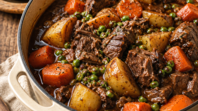 Homemade beef stew with tender beef, potatoes, carrots, peas, and rich brown gravy served in a rustic Dutch oven.