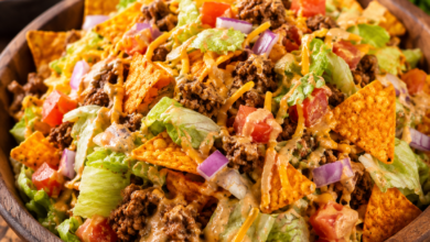 A large bowl filled with taco salad made from romaine lettuce, seasoned ground beef, diced tomatoes, shredded cheddar cheese, chopped red onion, creamy dressing, and crunchy Doritos.