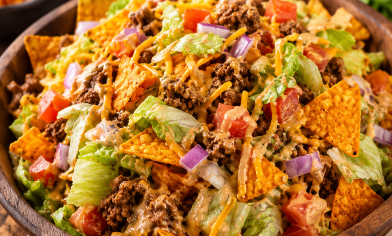 A large bowl filled with taco salad made from romaine lettuce, seasoned ground beef, diced tomatoes, shredded cheddar cheese, chopped red onion, creamy dressing, and crunchy Doritos.