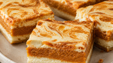 Sweet potato cheesecake brownies with creamy cheesecake layers, orange sweet potato filling, and a marbled top on a ceramic plate.