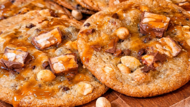 Bakery style Snickers cookies with gooey caramel, chocolate chunks, and peanuts on wooden board