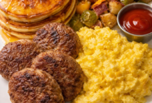 Classic American breakfast plate with pancakes, scrambled eggs, sausage, and crispy potatoes