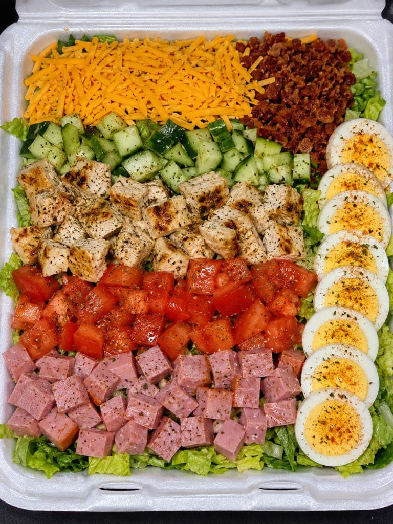 Restaurant-style classic Cobb salad with grilled chicken, bacon, ham, cheddar cheese, eggs, cucumbers, tomatoes, and romaine lettuce.