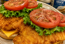 Crispy fried catfish sandwich with American cheese, lettuce, tomato, and Cajun tartar sauce on a toasted bun.
