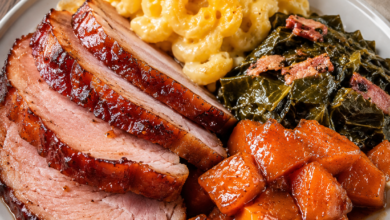Honey glazed baked ham served with creamy mac and cheese, Southern collard greens, and candied sweet potatoes on a white dinner plate.